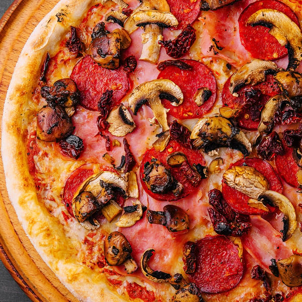 Close-up of a Maria's Kitchen pizza with pepperoni, mushrooms, and sun-dried tomatoes on a wooden board.