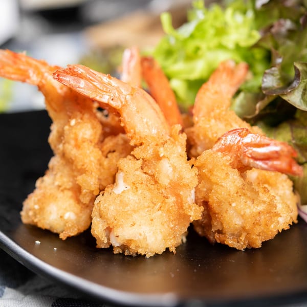 Crispy fried shrimp with tails on, served with fresh green lettuce on a black plate.