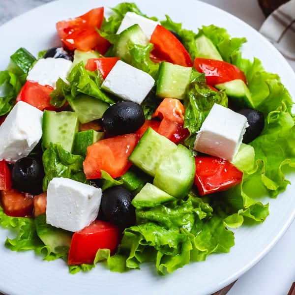 Fresh Greek salad with lettuce, tomatoes, cucumbers, black olives, and feta cheese on a white plate.
