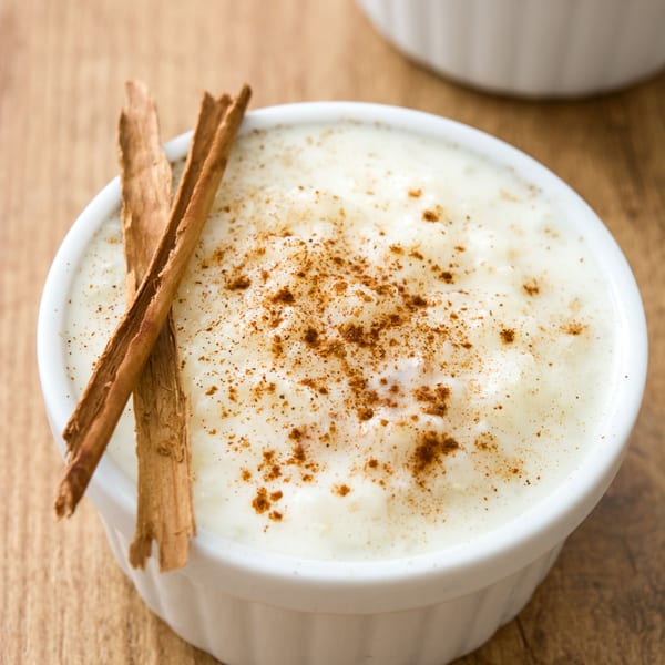 Creamy rice pudding topped with cinnamon powder and two cinnamon sticks in a white bowl.