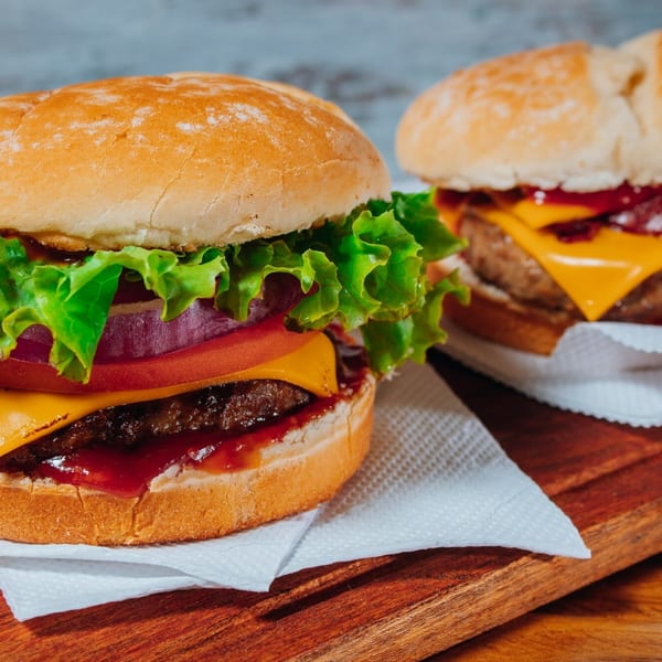 Two juicy burgers with cheese, lettuce, tomato, and onion on a wooden board.